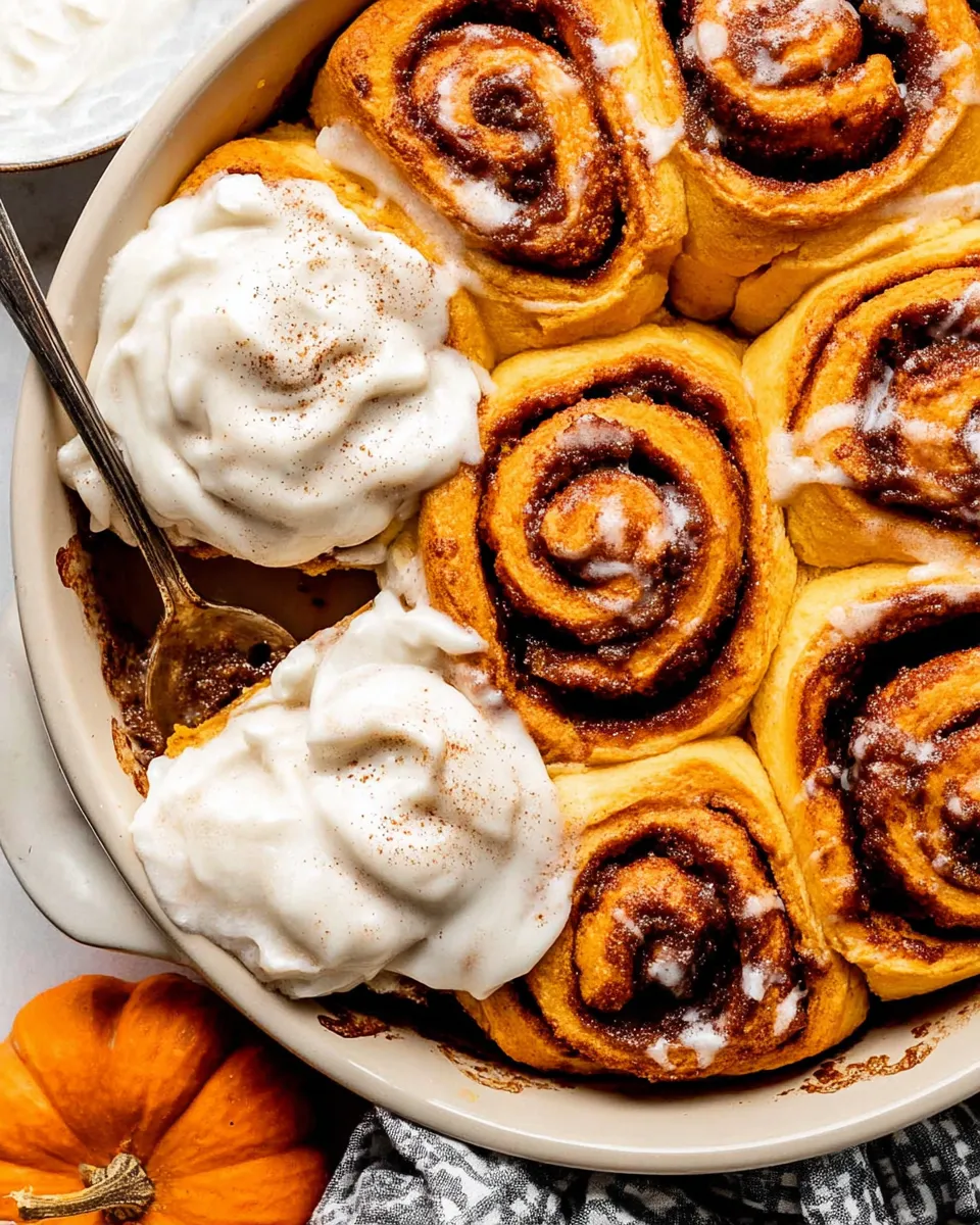 Soft pumpkin cinnamon rolls topped with cream cheese glaze, arranged on a rustic wooden board.