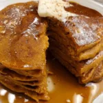 Stack of fluffy pumpkin pancakes topped with butter and maple syrup.