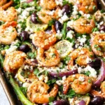 Sheet Pan Mediterranean Shrimp with roasted veggies, lemon slices, and fresh herbs on a baking tray.
