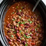 Bowl of slow cooker chili topped with cheese, sour cream, and cilantro.