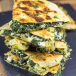 Crispy golden Spinach and Artichoke Quesadillas served with sour cream and salsa on a rustic plate.