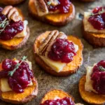 Sweet potato rounds topped with brie, cranberries, and pecans, served as a festive holiday appetizer.